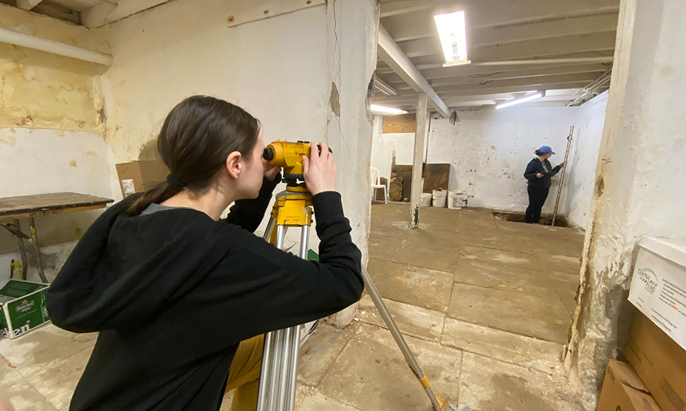 Two students on opposite sides of the room looking through surveying equipment.