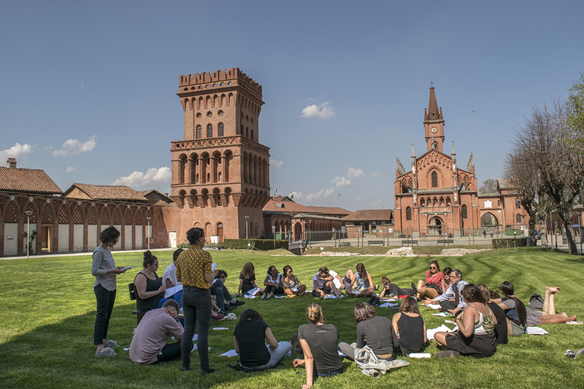 People sitting in a circle on grass outside a brick buidling.
