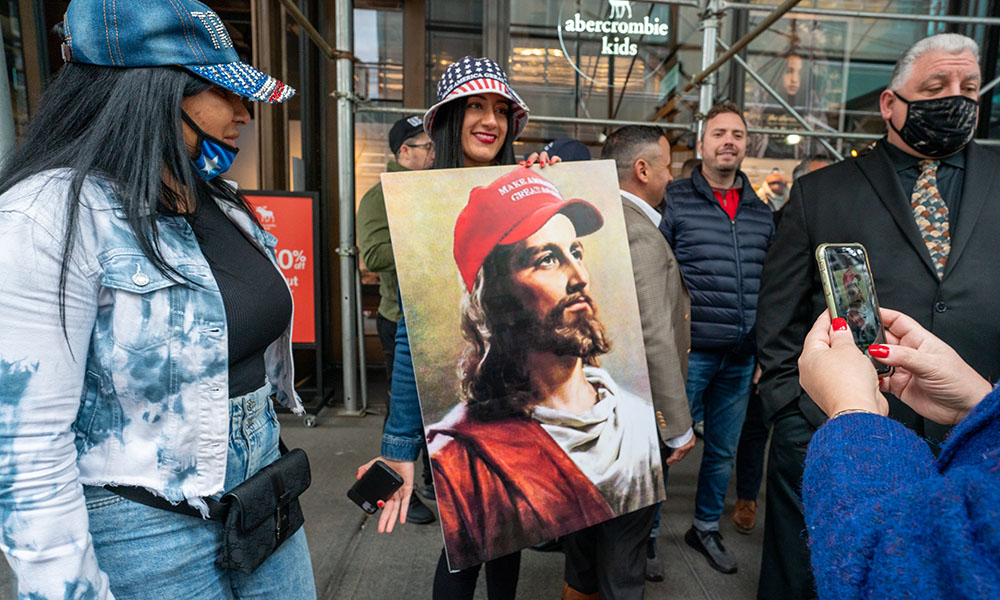 A woman holding a painting of Jesus with a Make America Great Again hat.