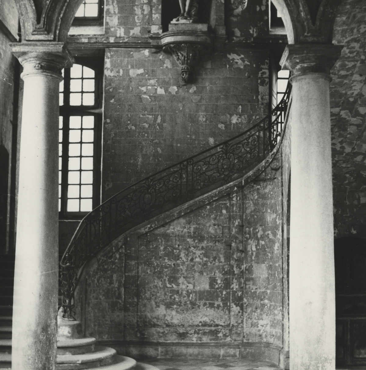 black and white photo of inside a building, the decorative iron railing of a staircase between two stone pillars