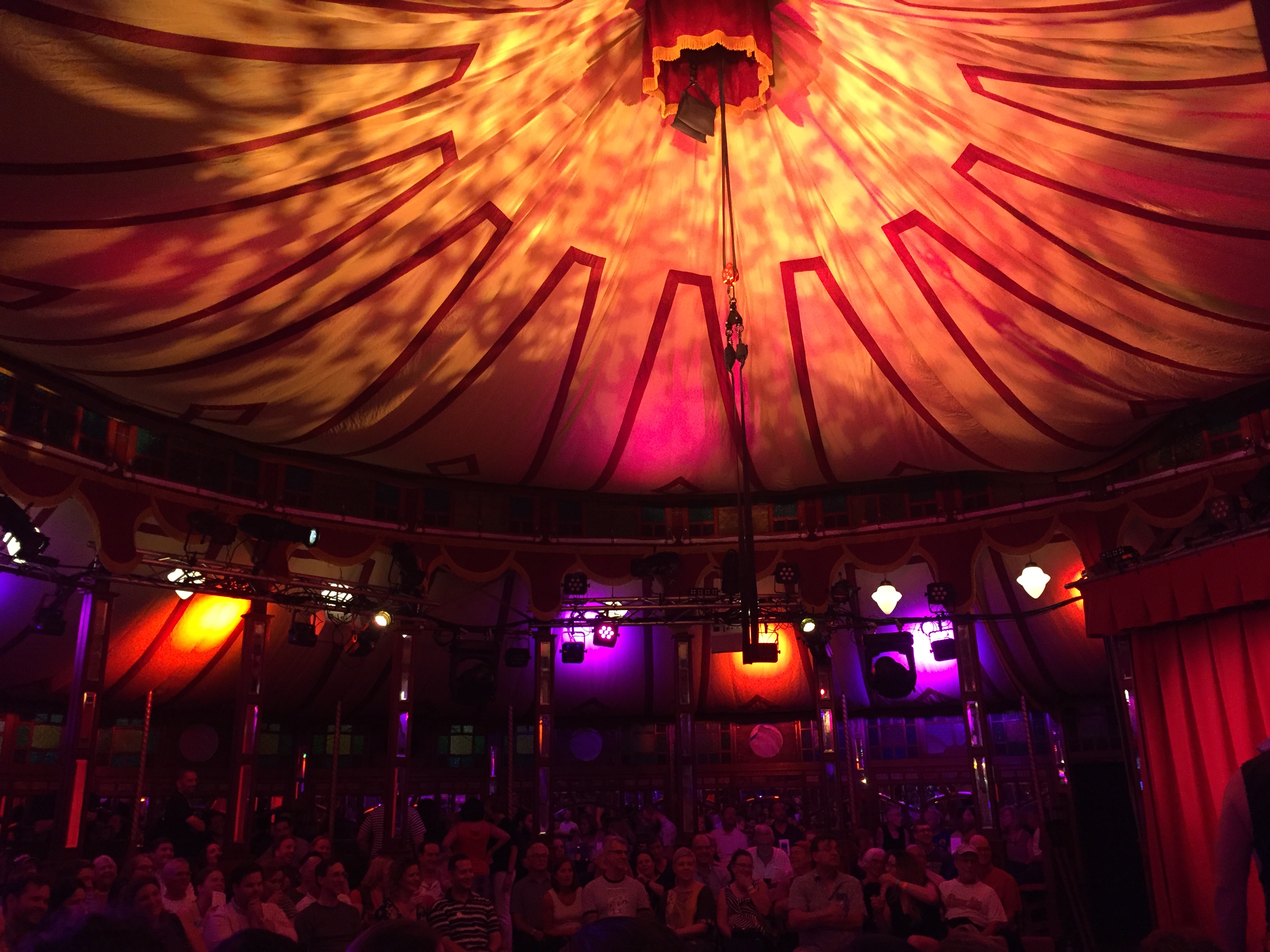 inside a tent a spiegeltent-fringe fest, lit with orange and purple spotlights