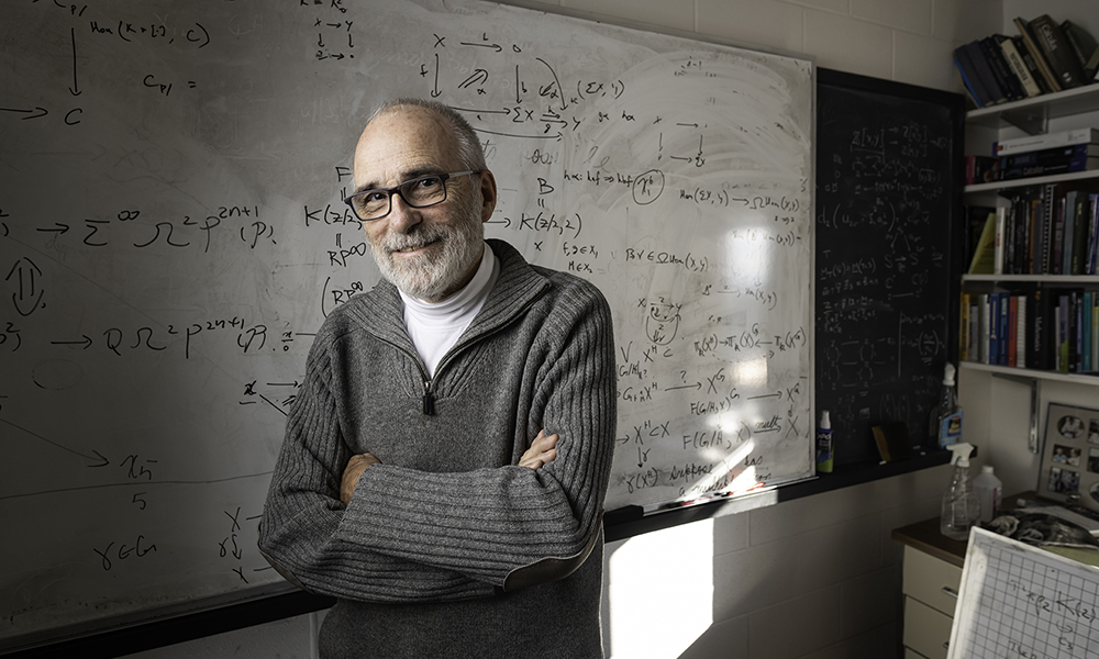 Doug Ravenel in his office standing in front of a white board containing math equations.