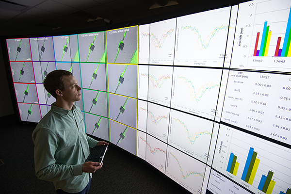 A student examining data sets on a large screen in a darkened room.