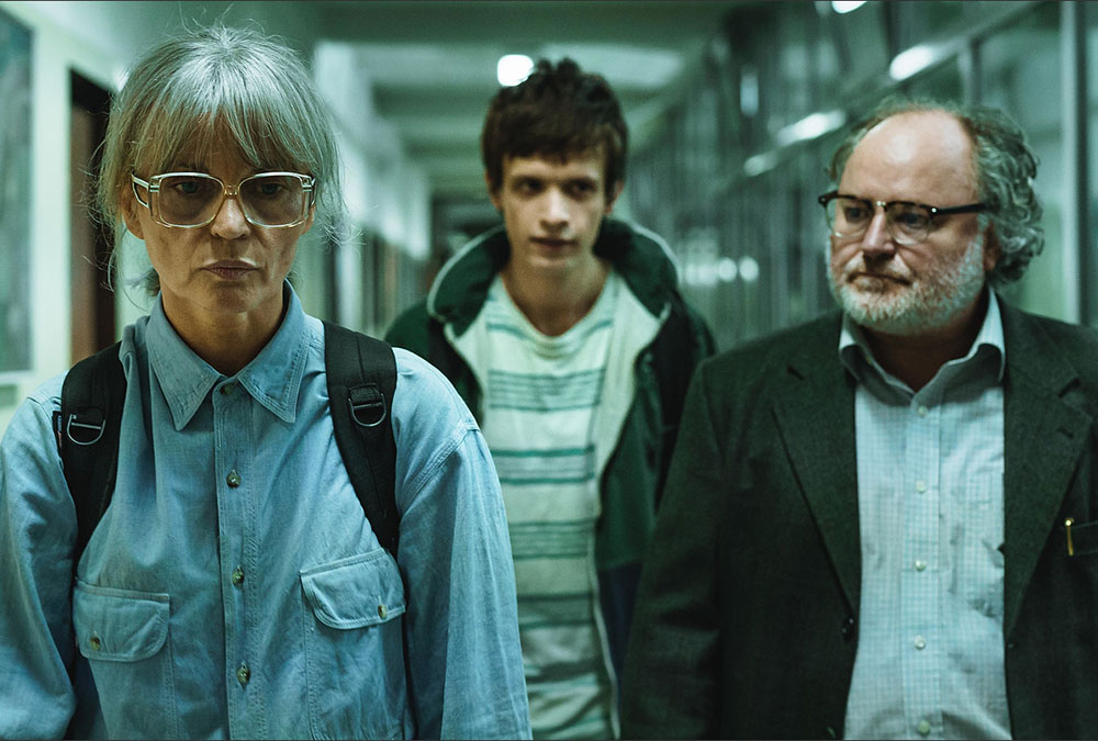 A still image from the movie of a man and woman walking down a hallway with a young man behind them.