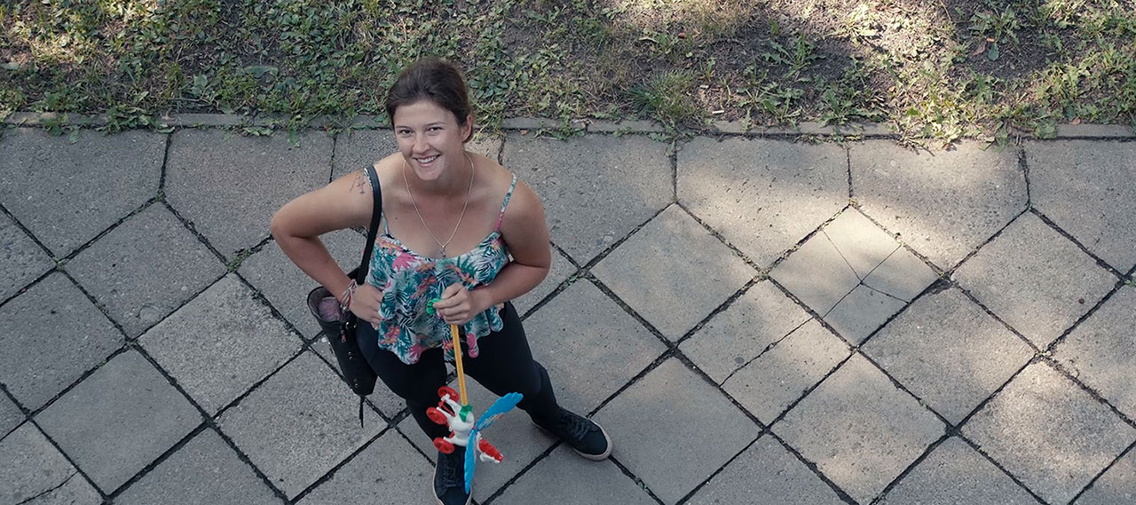 A still image from the film of a woman standing on a sidewalk looking up at the camera