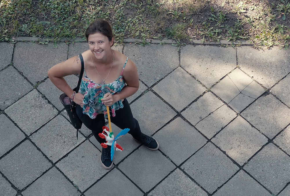 A still image from the film of a woman standing on a sidewalk looking up.