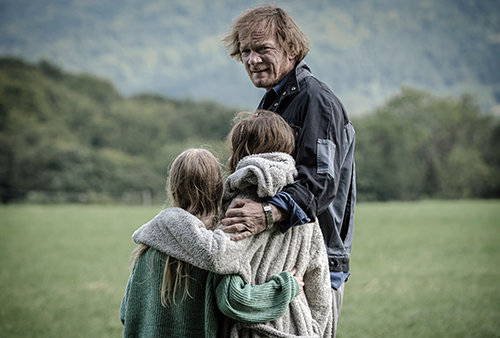 A still image from the film of a man with his arm around two young children.