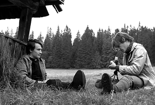 A still image from the film of two men sitting in a field. One man is playing an instrument.
