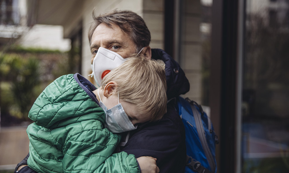 A man holding a small child. Both are wearing masks.