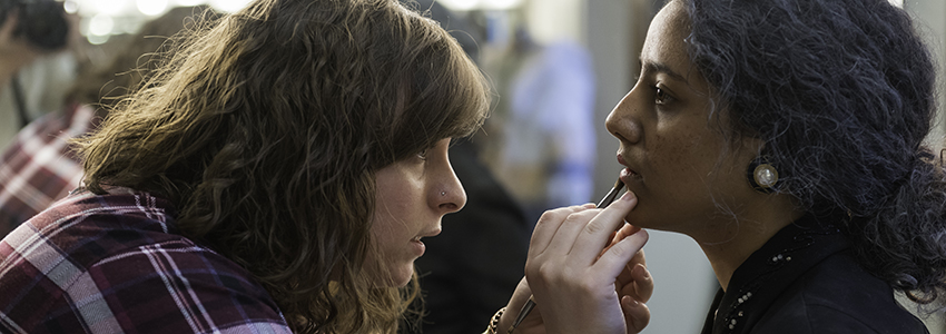 A student putting makeup on an actor.